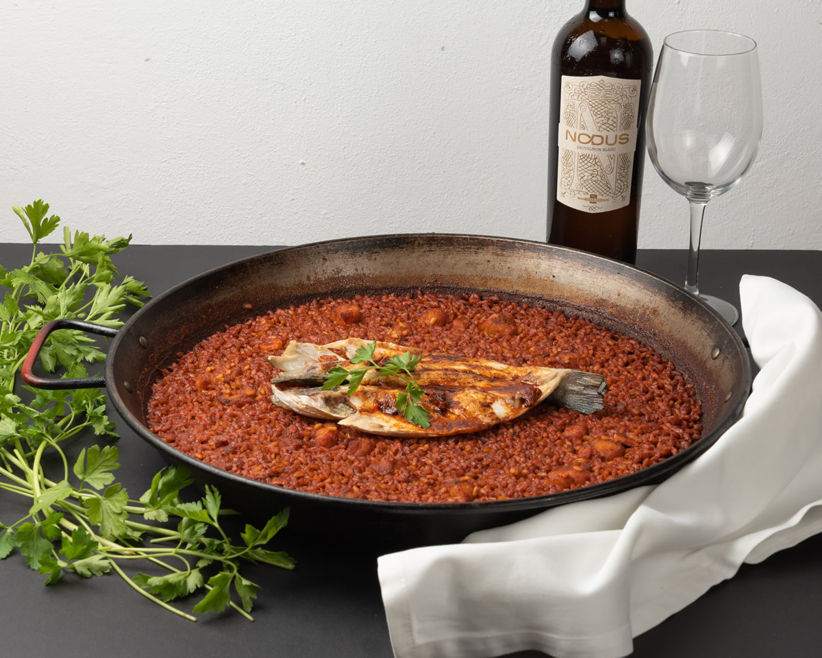 Arroz meloso rojo con pescado servido en paella
